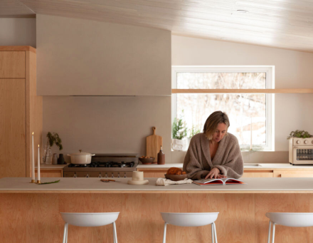 Une personne préparant des aliments dans une cuisine moderne et chaleureuse. L’espace met en valeur des matériaux naturels comme le bois clair et un design épuré. On aperçoit une cuisinière, un four de Our Place, et des accessoires de cuisine soigneusement sélectionnés, créant une atmosphère conviviale et fonctionnelle.