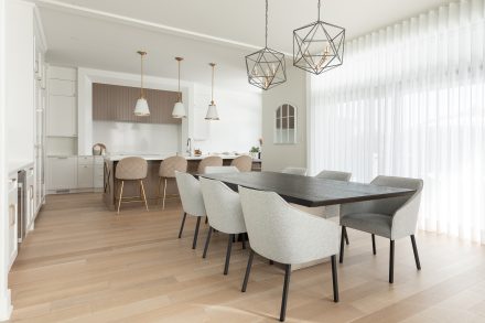 Un espace salle à manger accueillant avec une grande table en bois foncé entourée de chaises en tissu gris clair. Les suspensions géométriques en métal noir ajoutent une touche moderne, tandis que les rideaux vaporeux laissent entrer une lumière naturelle douce.